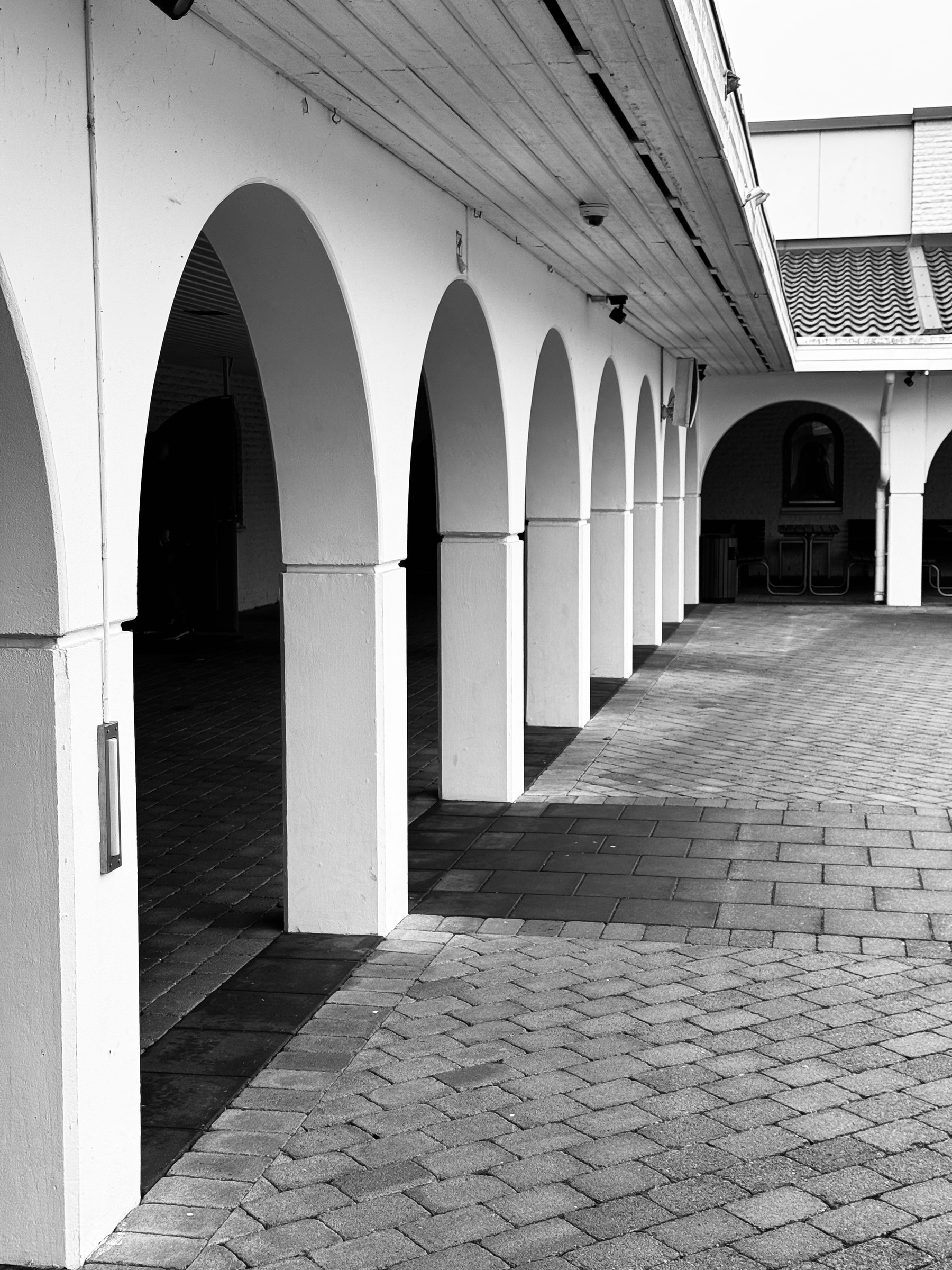 A series of white arches creates a corridor effect in a paved courtyard.