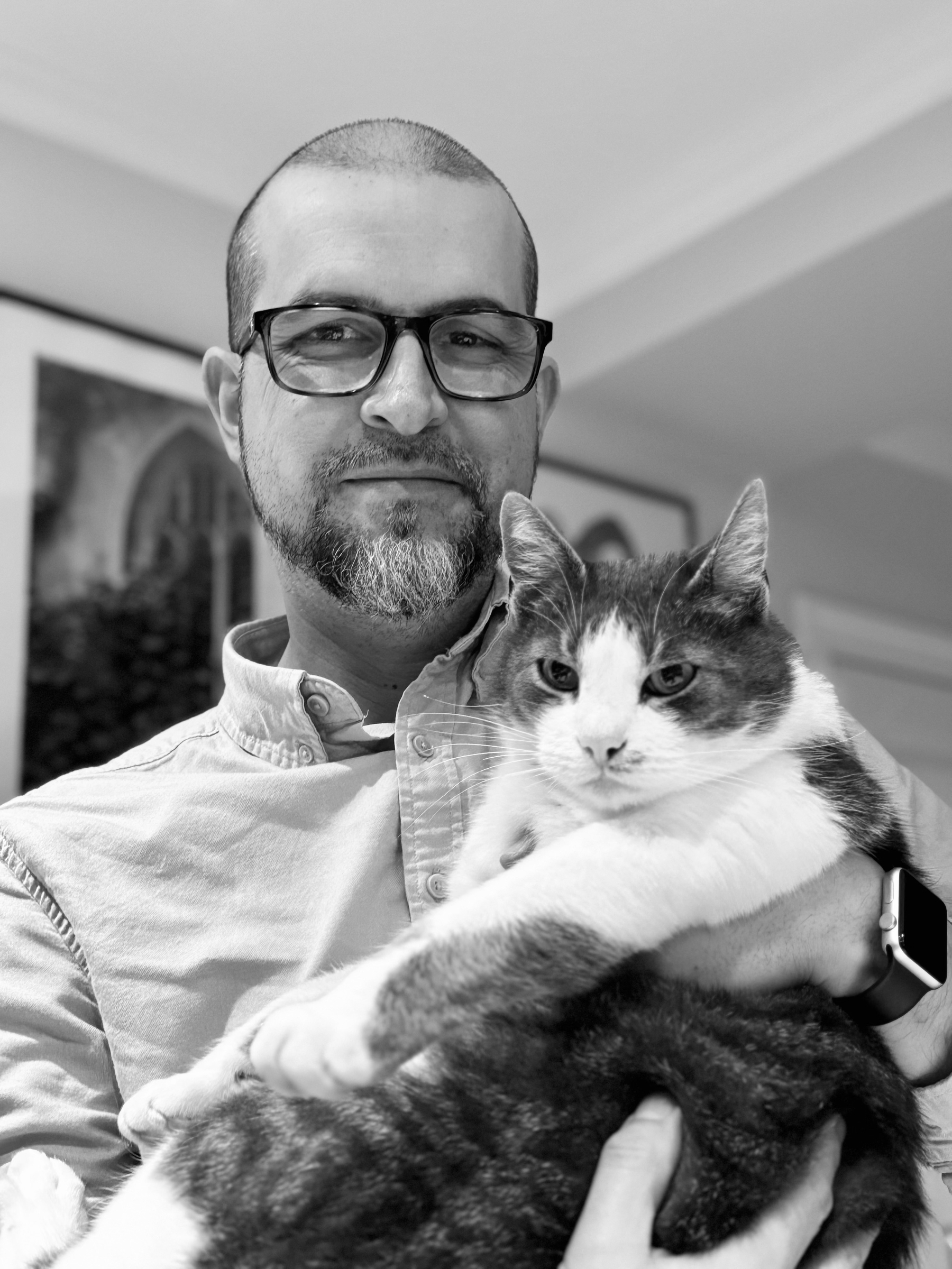 En man med glasögon håller en katt i sin famn.