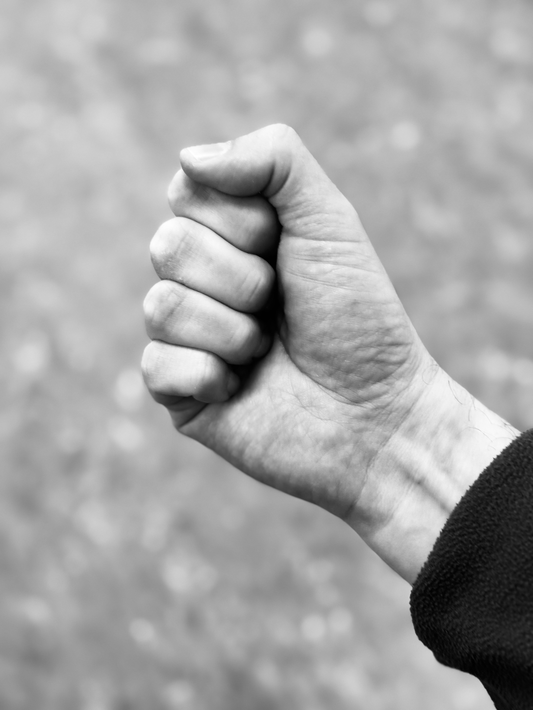 Auto-generated description: A tightly closed fist is held up against a blurry background in black and white.