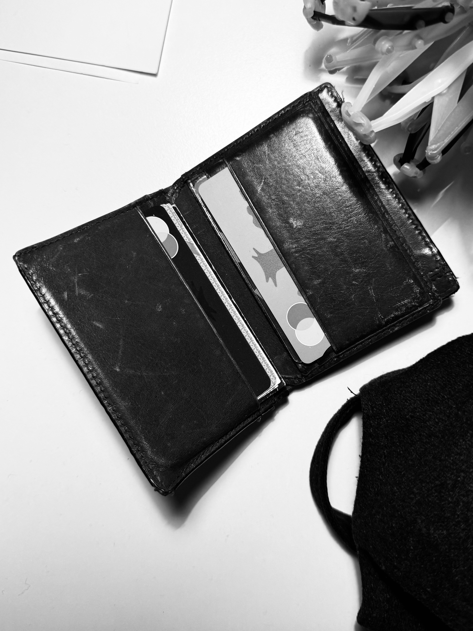 A black wallet with several cards is open on a white surface alongside a black fabric item and some plastic hangers.